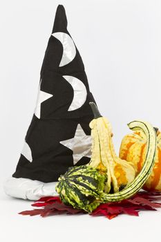 Wizard's hat with stars and moon placed behind decorative gourds on red, autumn leaves