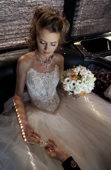 The bride with a crystal shoe. The bride in a wedding dress sits in a limousine holds a crystal shoe.