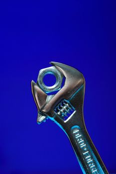 Extreme closeup of adjustable wrench gripping a screw nut on blue background