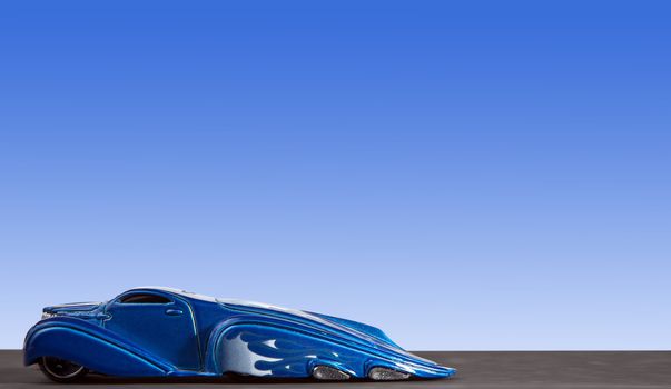 Beautiful blue American HotRod car speeding across asphalt with clear sky backdrop