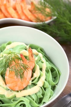 Green tagliatelle (ribbon noodle) with a cream sauce, shrimp and fresh dill served in a bowl (Selective Focus, Focus on the front of the shrimp)