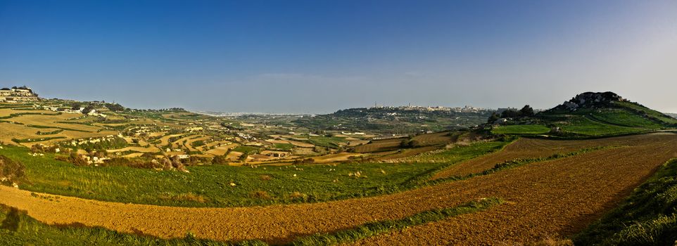 Panorama of a Maltese landscape showing a Bronze Age setllement hill on the right with Fort Dwejra on extreme left and Mtarfa in the background