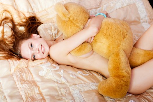 pretty nude woman lies on bed and embreces a teddy bear