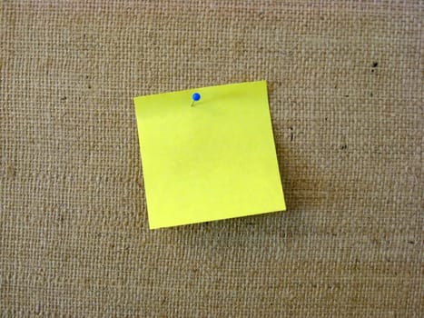 Yellow note paper with pin on fabric background
