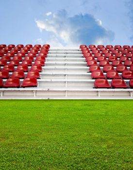 Red bleachers in the arena with green field and sky background