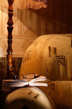 Home interior with luminous floor lamp near armchair. Open book and spectacles lying on armchair