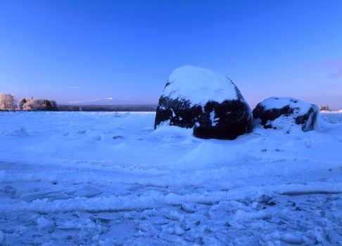 Winter landscape with big snowy stone by the lake