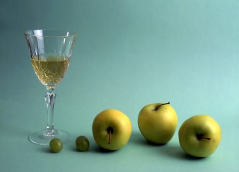 A glass of white wine with fruits isolated on green background