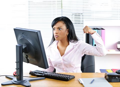 Angry young black business woman punching computer in office