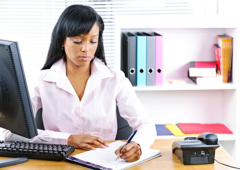 Serious young black business woman writing at desk in office