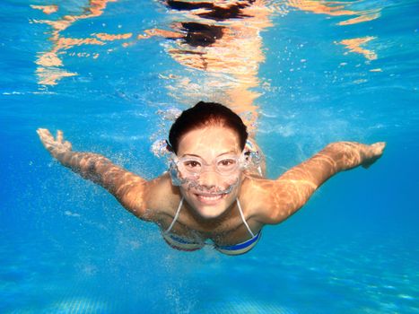 Woman swimming underwater in pool smiling. Young female swimmer with swim goggles at holiday resort.