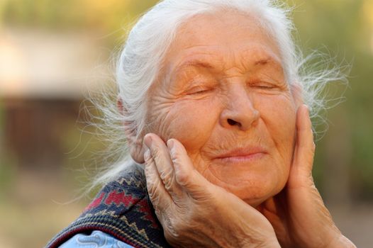 The elderly woman with closed eyes. A photo outdoors