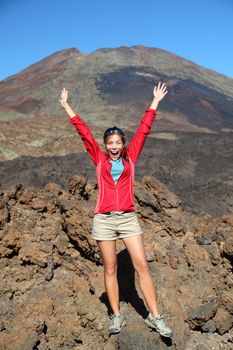 Portrait of happy hiker with arms raised in air with conquered mountain behind. Mountain volcano Pico Viejo on Teide, Tenerife, Canary Islands, Spain.