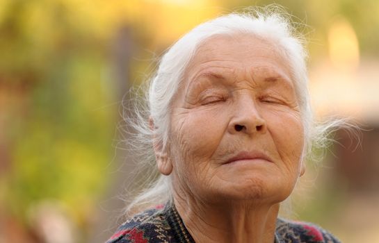 The elderly woman with closed eyes. A photo outdoors