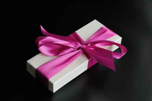 Gift box with a big pink bow. On a dark background.