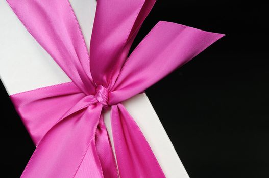 Gift box with a big pink bow close up. On a dark background.