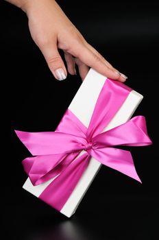 Gift box with a big pink bow and woman's hand. On a dark background.