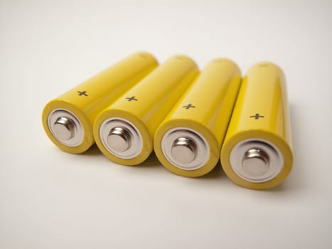 Four yellow batteries with the contacts and the plus sign showing, grey background