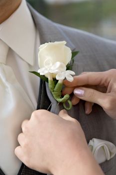 Woman attaching a white bouttonniere to man's gray suit