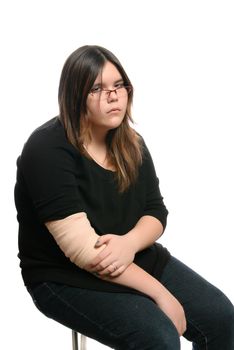 A bored teenage girl is tired of having an injured elbow, and is sitting on a stool, isolated against a white background.