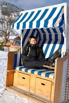 Young woman sleeping in roofed wicker beach chair on a sunny winter day in austria.