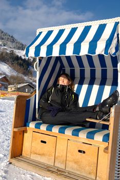 Young woman sleeping in roofed wicker beach chair on a sunny winter day in austria.