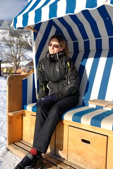 Young woman relaxing in roofed wicker beach chair on a sunny winter day in austria.