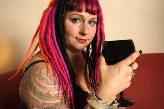 Portrait of a beautiful female goth sitting on a red couch drinking from a black wine glass.  Shadow depth of field, focus on the right eye.
