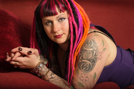 Portrait of a beautiful female goth with dreadlocks on a red couch.
