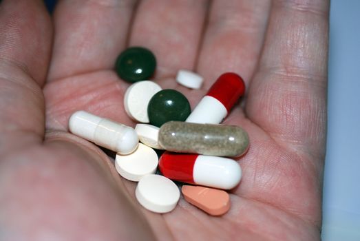 A hand holding an array of medicinal tablets and capsules