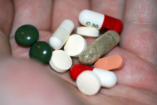 A hand filled with tablets, capsules and pills.