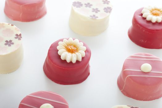 Several pink petits fours with various decorations.