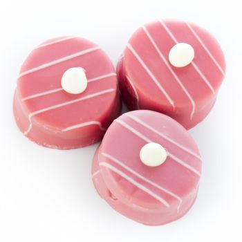 Three pink petits fours on white surface.