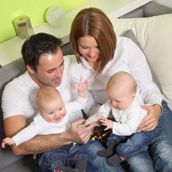 Young family with two children sitting at home on the couch and play with the children

