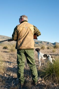 Quail hunter in camouflage clothing walking across the field