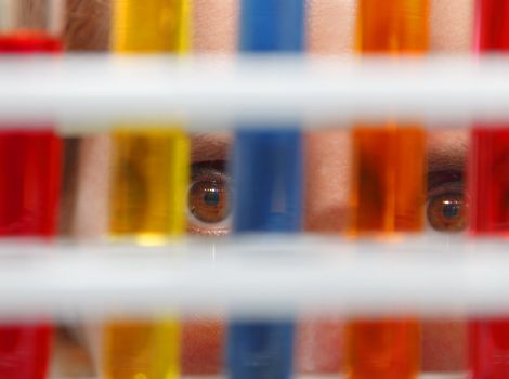 Close-up image of a person's eyes looking through test tubes containing solutions in a laboratory.