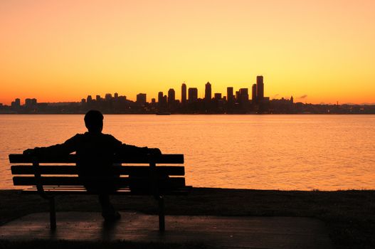 silhouette of a man sitting on a park bench watching the sun rise behind Seattle skyline