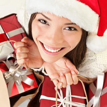 Christmas gifts santa woman shopping. Closeup portrait of young woman holding christmas presents in shopping bags. Beautiful smiling happy santa girl wearing santa hat.