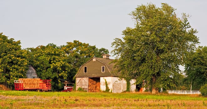 A barn in the country with a trailer full of hay. Photo was captured in late evening sunlight.
