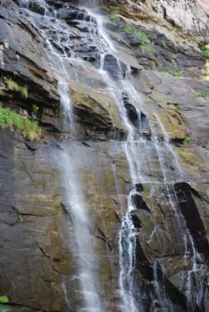 Thin streams of water running down on rocks in mountain waterfall