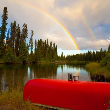 Overturned canoe with coffee mugs under bright rainbow