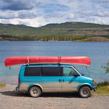 Dirty blue minivan with red canoe on roofrack