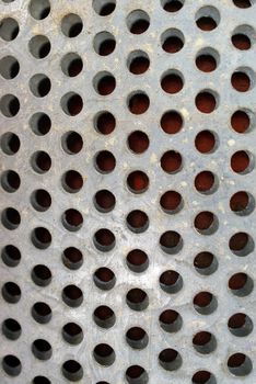 A metal surface with round holes and some sand on it. 