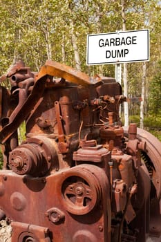 Big rusty diesel engine block in front of sign posting "Garbage Dump"