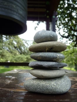 Zen stones on a peace of wood next to a japonese bell in a park