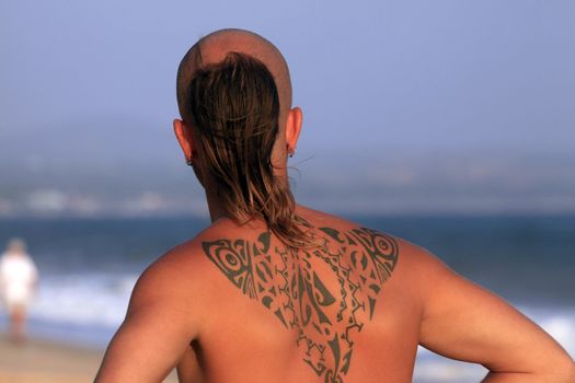 The young man with a beautiful tattoo on a coast of ocean