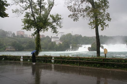 Alone in rain by Rhine waterfall with blue umbrella