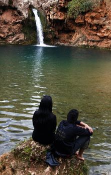 Two persons, one female and one male, watching a beautiful waterfall.