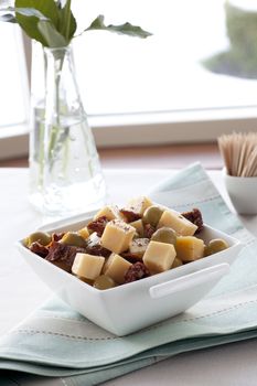 Cheese, sun dried tomatoes and olives in a white square bowl.