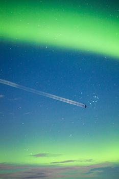 Airplane on moon lit night sky with intense Aurora borealis display and lots of stars.